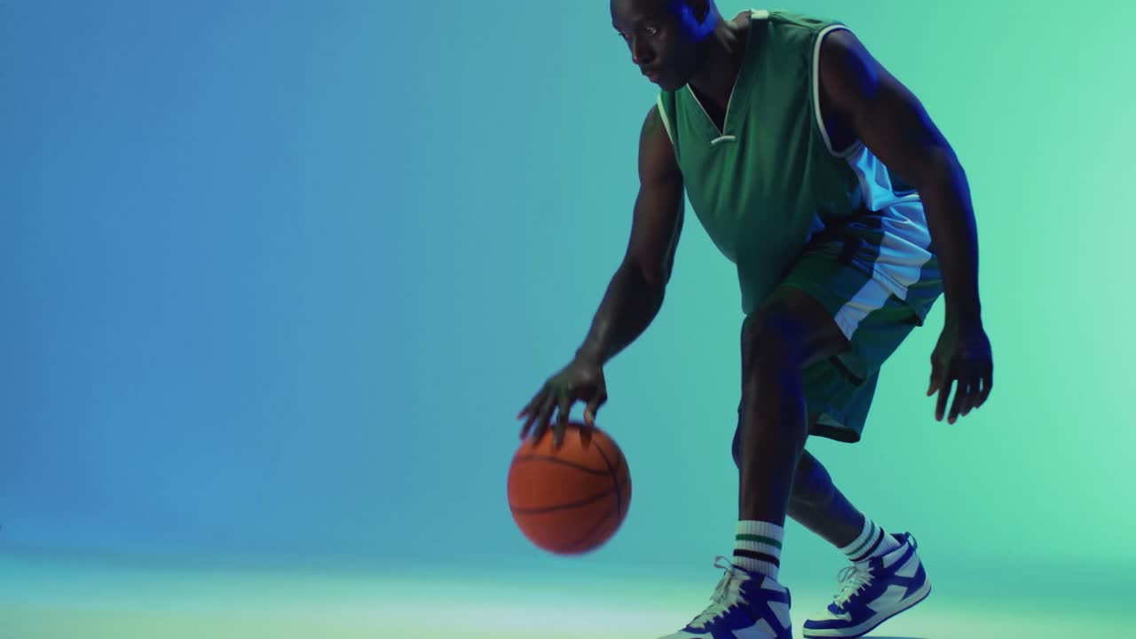 Video of african american male basketball player bouncing ball on blue background