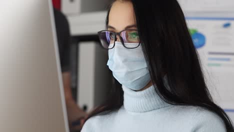 woman in face mask and glasses working on computer in office