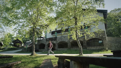 a young hiker is passing a mountain cottage, past hte trees