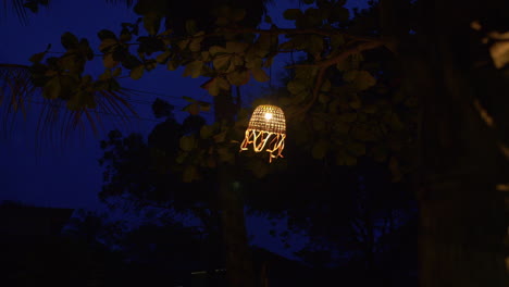 Lantern-with-paper-ribbons-hanging-from-tree-and-moving-in-the-wind-on-dark-blue-background