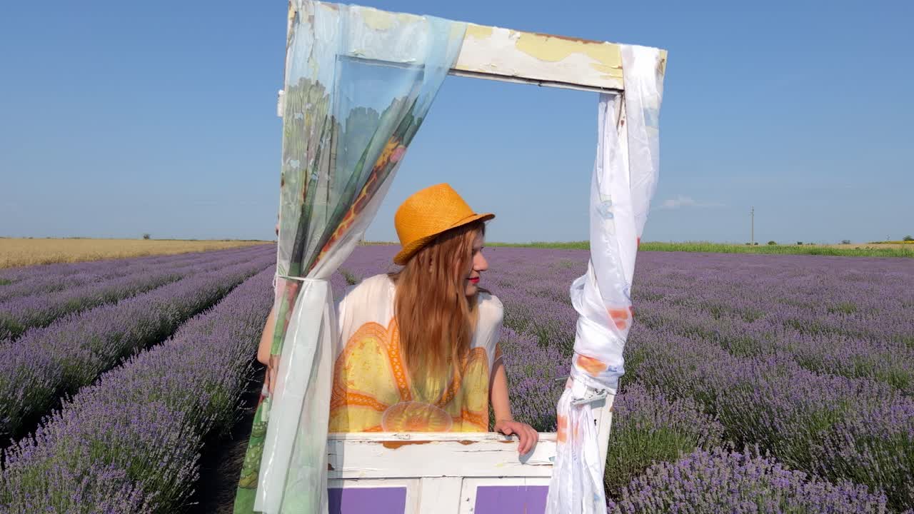 Piano medio di giovane donna in stile hippie appoggiata a una porta decorativa in un campo di lavanda e che si guarda intorno.