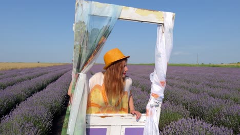 medium shot of young woman in hippie style leaning against decorative door in lavender field and looking around