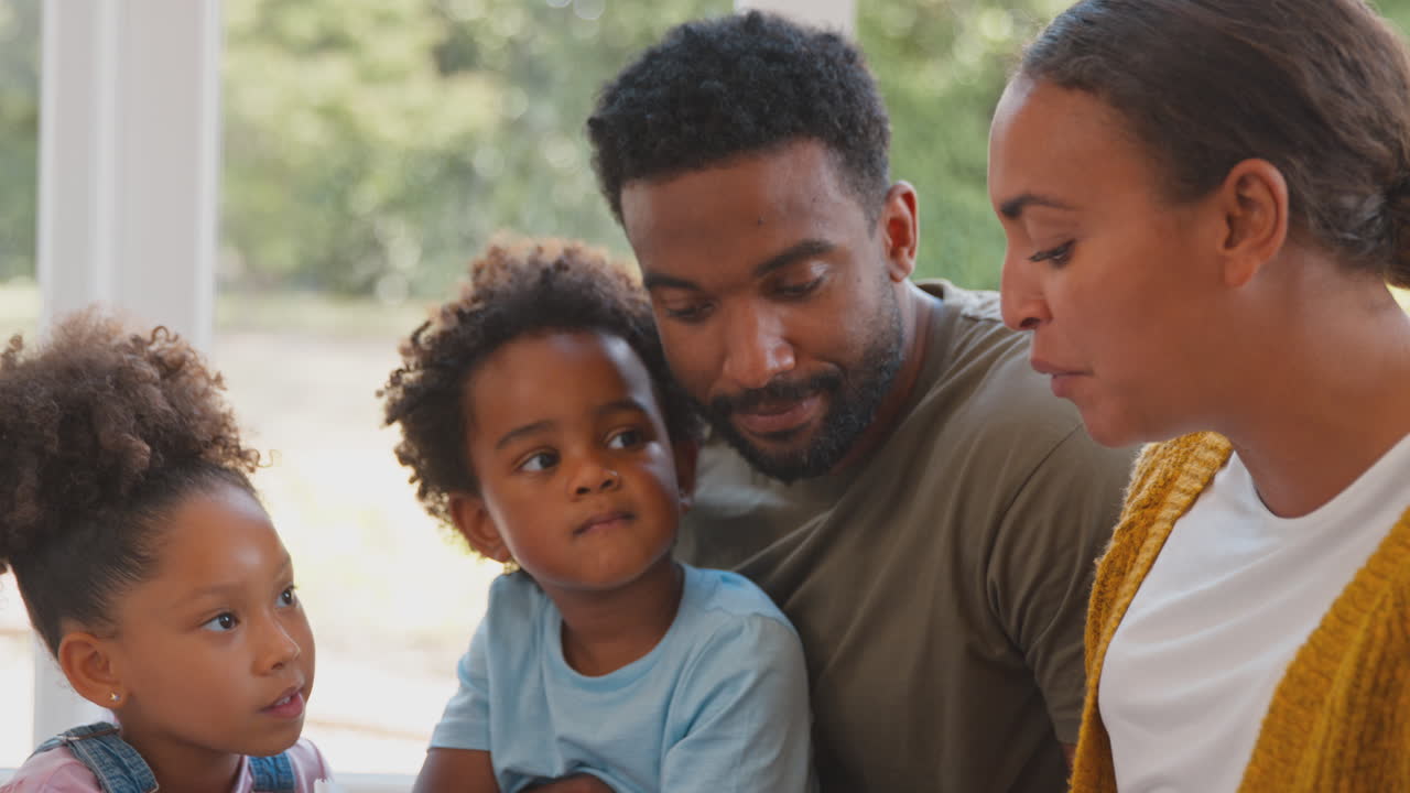 Famiglia seduta sul pavimento nel soggiorno di casa che legge un libro insieme.