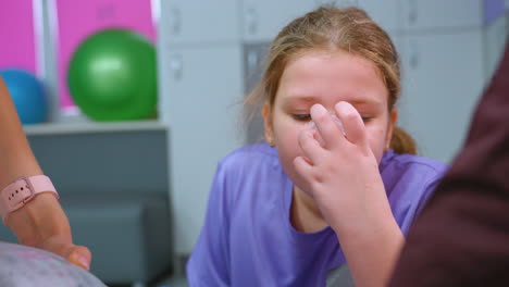 primer plano de un niño con una camisa púrpura bebiendo agua de una taza transparente, con una vista parcial de la mano de una persona que lleva un reloj inteligente vertiendo agua, mientras que otra persona es parcialmente visible