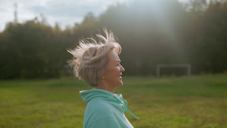 canine specialist joyfully running across green sunny field wearing sports hoodie, smiling happily with breeze blowing hair, enjoying vibrant outdoor atmosphere during energetic morning activity