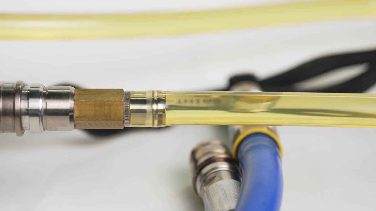 Macro close-up of liquid cooling system components featuring transparent yellow coolant tube, brass fittings, stainless steel quick-connect couplings and blue hose
