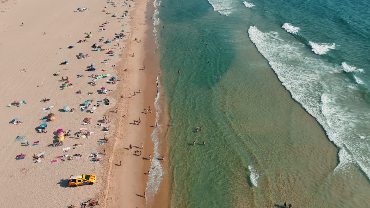 Vista aérea de uma praia lotada com pessoas aproveitando o sol e o oceano