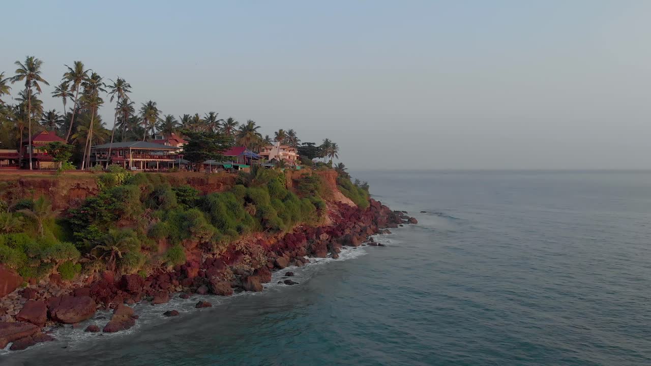 Veduta aerea della spiaggia di Varkala, Kerala, India, che mostra resort e caffè su falesie verdi e fitte lungo la costa, con la bassa marea che si infrange su di esse.