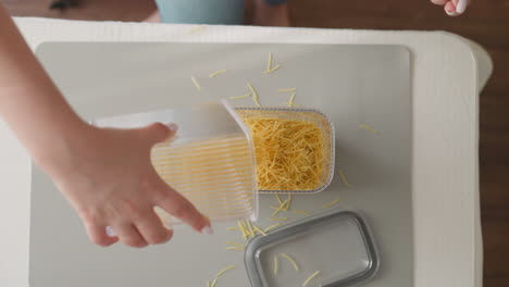 woman pours spaghetti and covers plastic container with lid