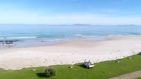 drone shot of guy sitting on his land rover with surfboard looking out to sea at the potential surf