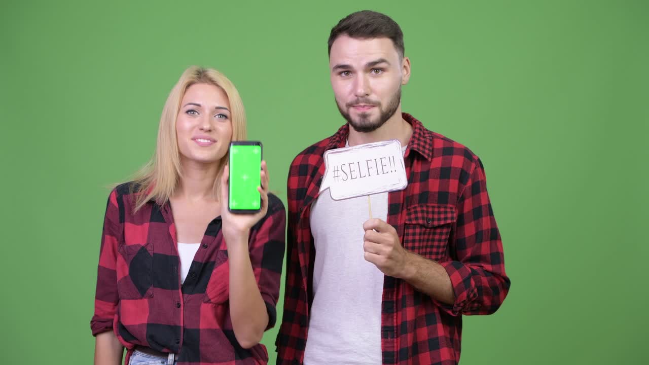 Young couple showing phone while holding selfie paper sign together