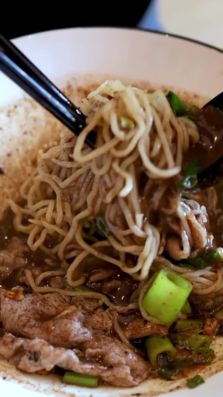 Un primo piano di bacchette che sollevano vermicelli di riso da una ricca ciotola di zuppa di noodle di maiale
