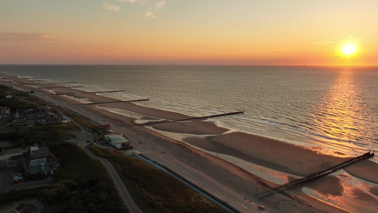 toma aérea sobrevolando un pequeño pueblo costero a lo largo de una playa con groynes durante una hermosa puesta de sol sin nubes en verano