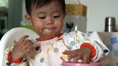 adorable asian baby girl playing with spoon and food after eating at home