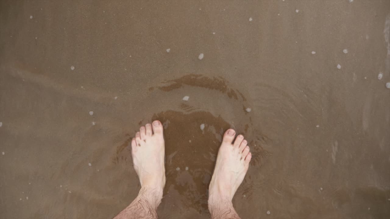 밀물이 들어와 해안에 물이 찰 때 남자의 발이 해변에 서 있었다