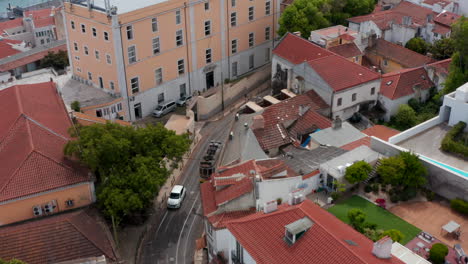 Aerial-view-of-tramway-driving-in-town-streets.-Drone-camera-tilts-up-to-city-panorama-with-long-bridge-over-river.-Lisbon,-capital-of-Portugal.