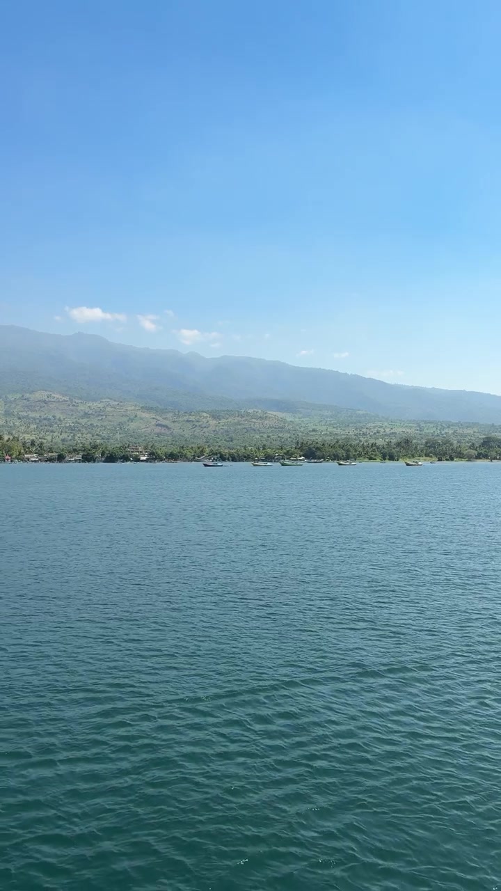Vista panorâmica de águas azuis calmas com montanhas distantes e barcos