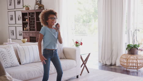 Niña-Afroamericana-Preadolescente-Bailando-Y-Cantando-En-Casa-Usando-El-Teléfono-Como-Micrófono,-Tres-Cuartos-De-Longitud