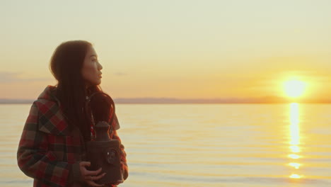 young woman holding vintage lantern, enjoying beautiful sunset by lake