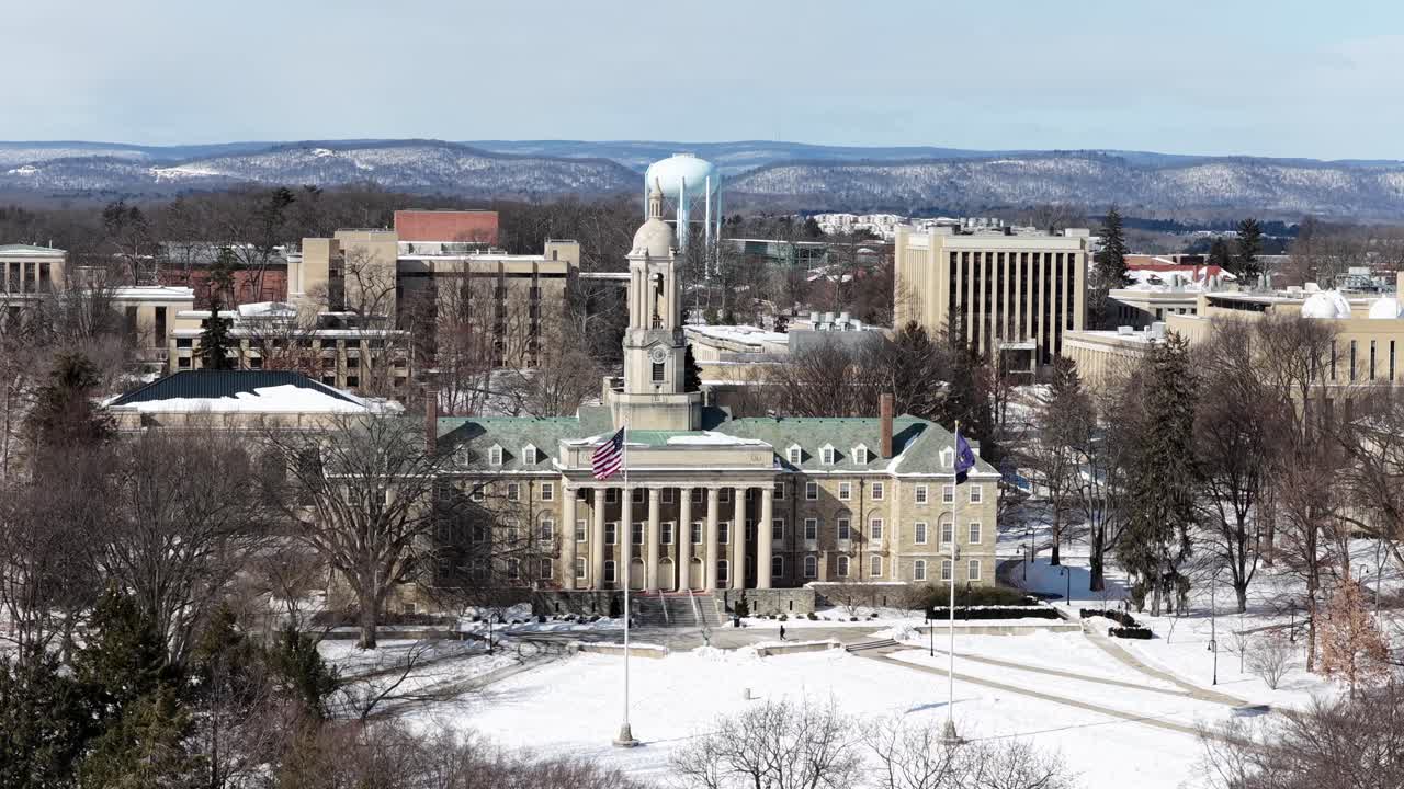 Indledende droneoptagelse af det historiske Penn State University i USA på en solrig vinterdag. Viftende flag fra USA og Pennsylvania. Sneklædte marker ved indgangen. Nærmende droneflyvning.