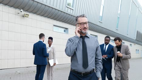 gray-haired businessman wearing glasses and talking on the phone while walking down in the street