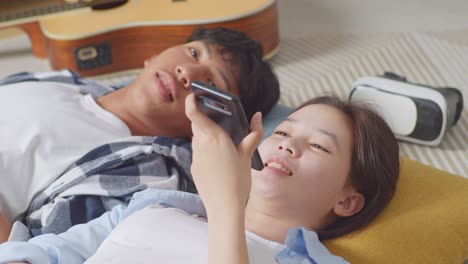 close up of asian teen couple recording voice message on smartphone while lying on carpet on the floor at home