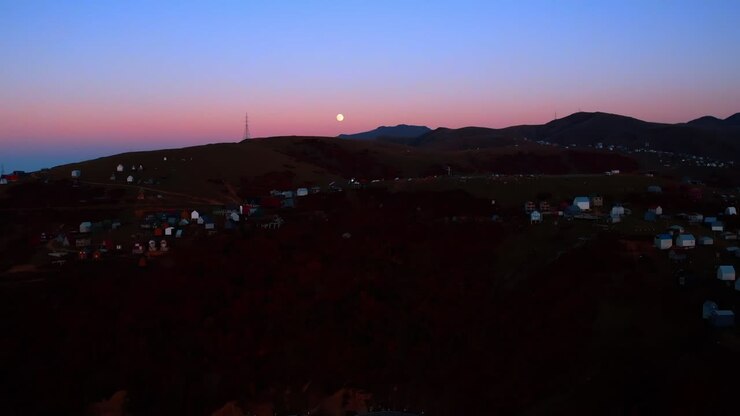 Avvicinandosi alle rocce con numerose case sui pendii. La luna splende nel cielo rosa-blu sullo sfondo