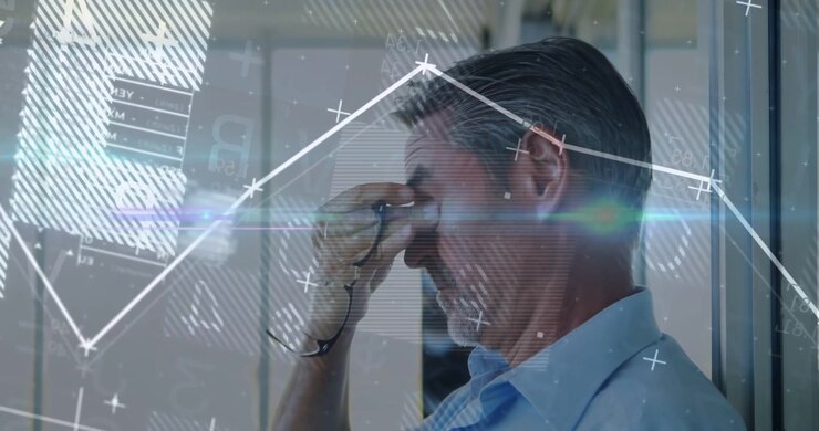 Direttore d'ufficio uomo appoggiato a una parete di vetro, si toglie gli occhiali e si strofina il naso mentre i grafici HUD impennano.
