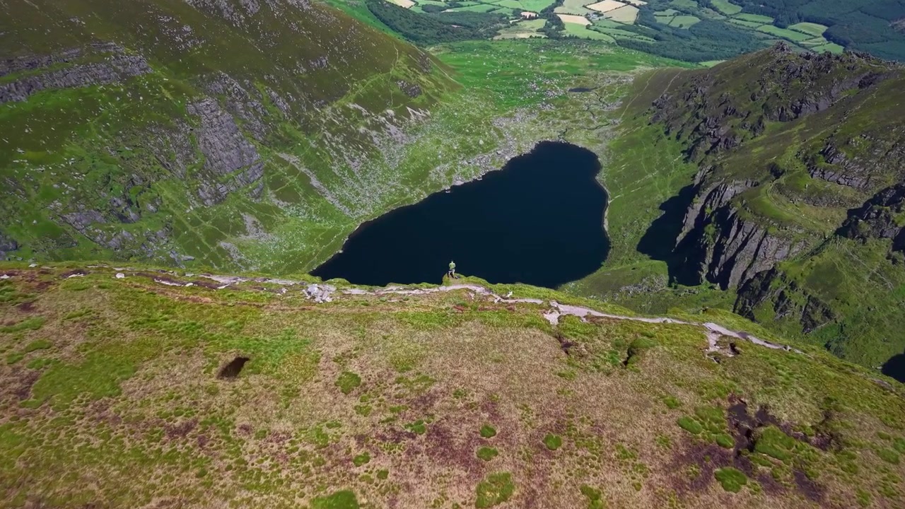 Vista aerea di un uomo che osserva il Lago Counshingaun e il paesaggio irlandese da una scogliera. Escursionismo