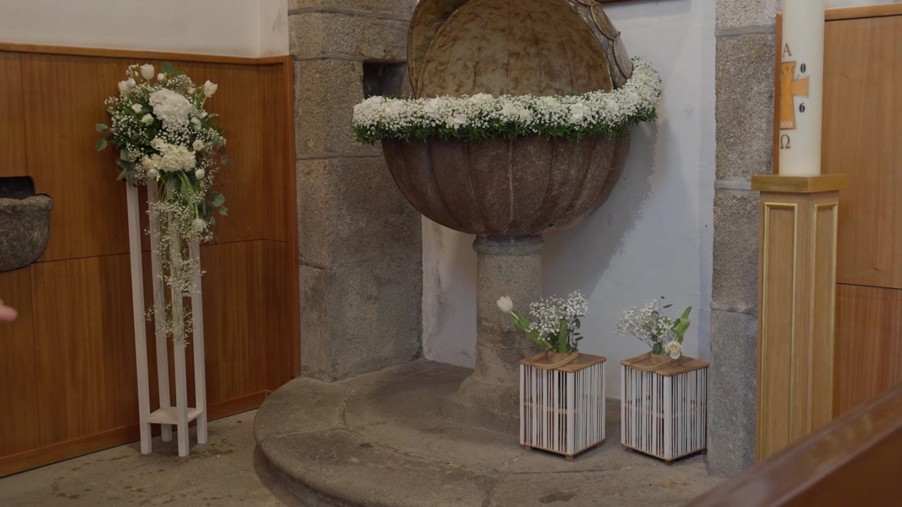 Fonte battesimale rotonda adornata con fiori bianchi accanto al cero pasquale all'interno