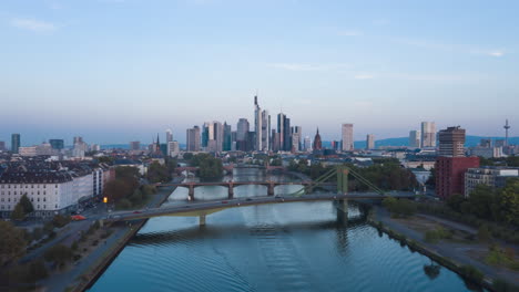 Frankfurt-am-Main,-Germany-Skyline-Establisher-Hyperlapse-moving-Time-Lapse-over-Main-River-with-cargo-Ship,-Aerial-backwards-4K