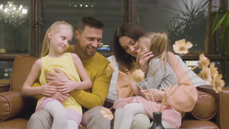 happy parents sitting on sofa with their two little girls and spending time together at home