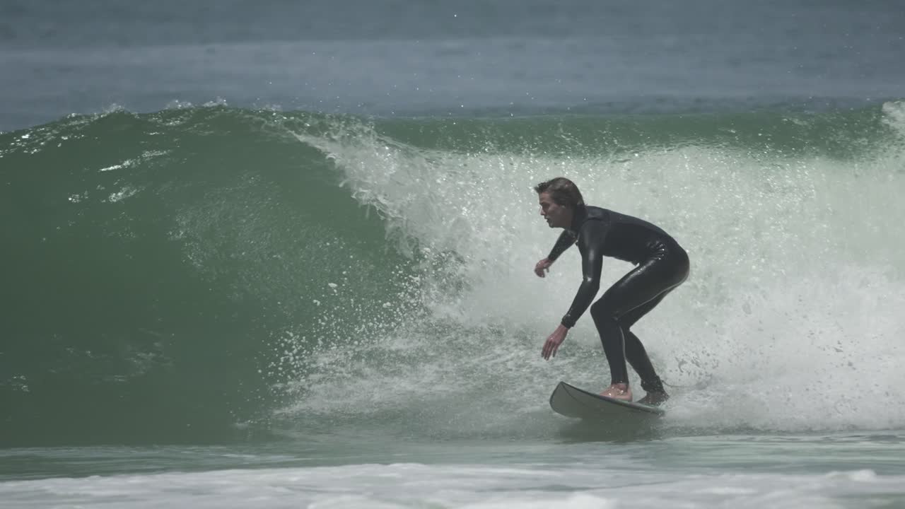 A young surfer performs an aerial maneuver above a powerful wave, frozen mid-flight with water spray exploding beneath