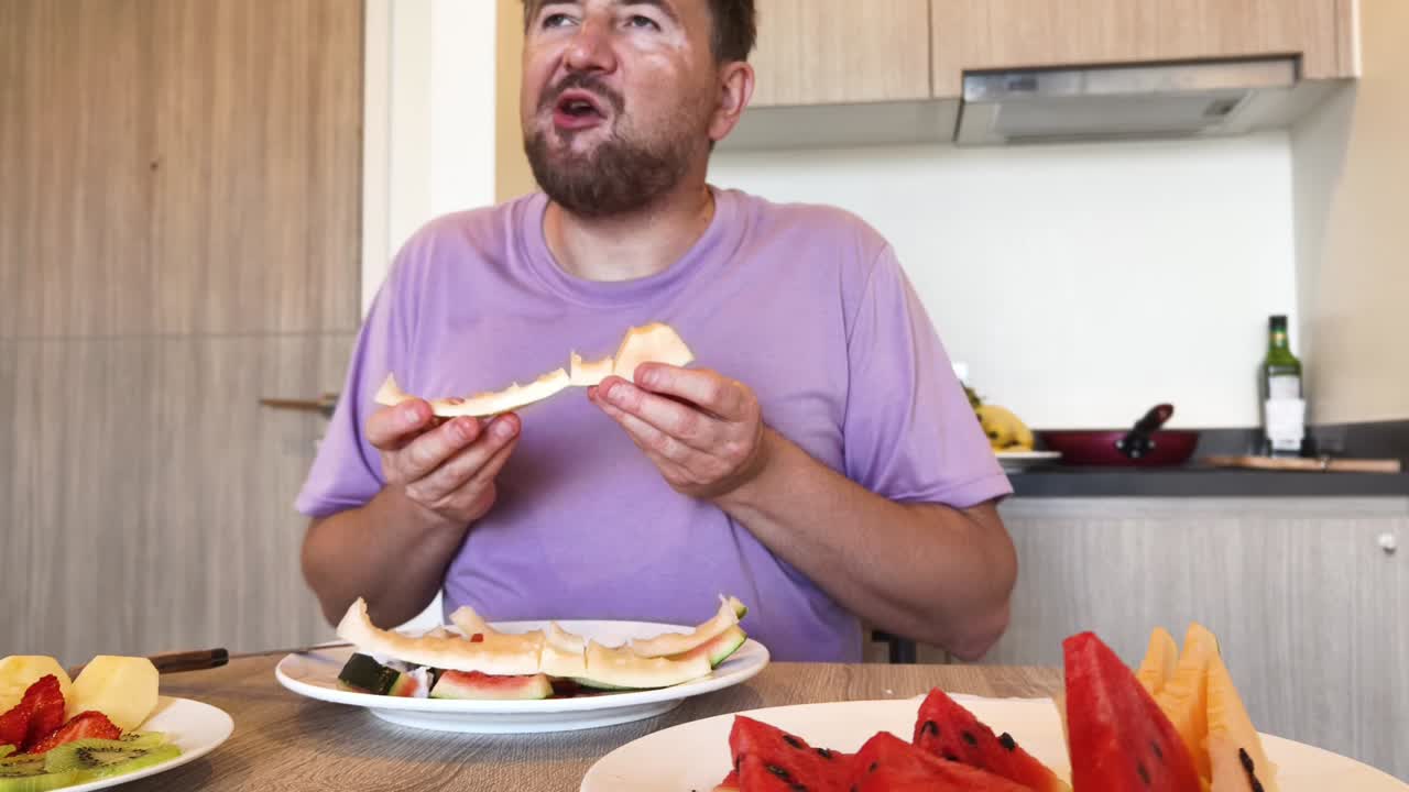 Man eating watermelon and other fruits in the kitchen