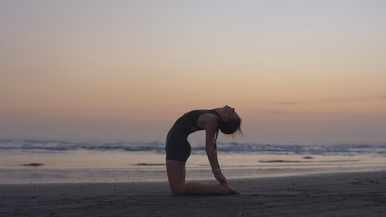 Woman practicing yoga at sunrise on the beach