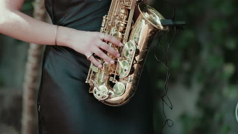 close up of woman in black dress playing golden saxophone with attached microphone