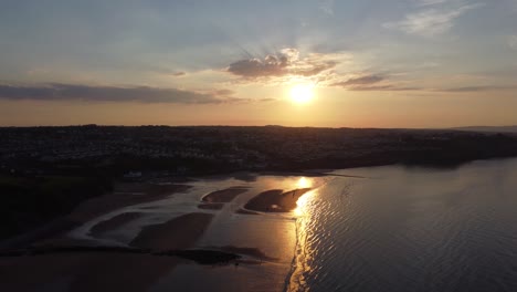 Sunset-rays-beam-fiery-golden-colours-across-relaxing-beach-ocean-coastline-aerial-view-slow-left-drift