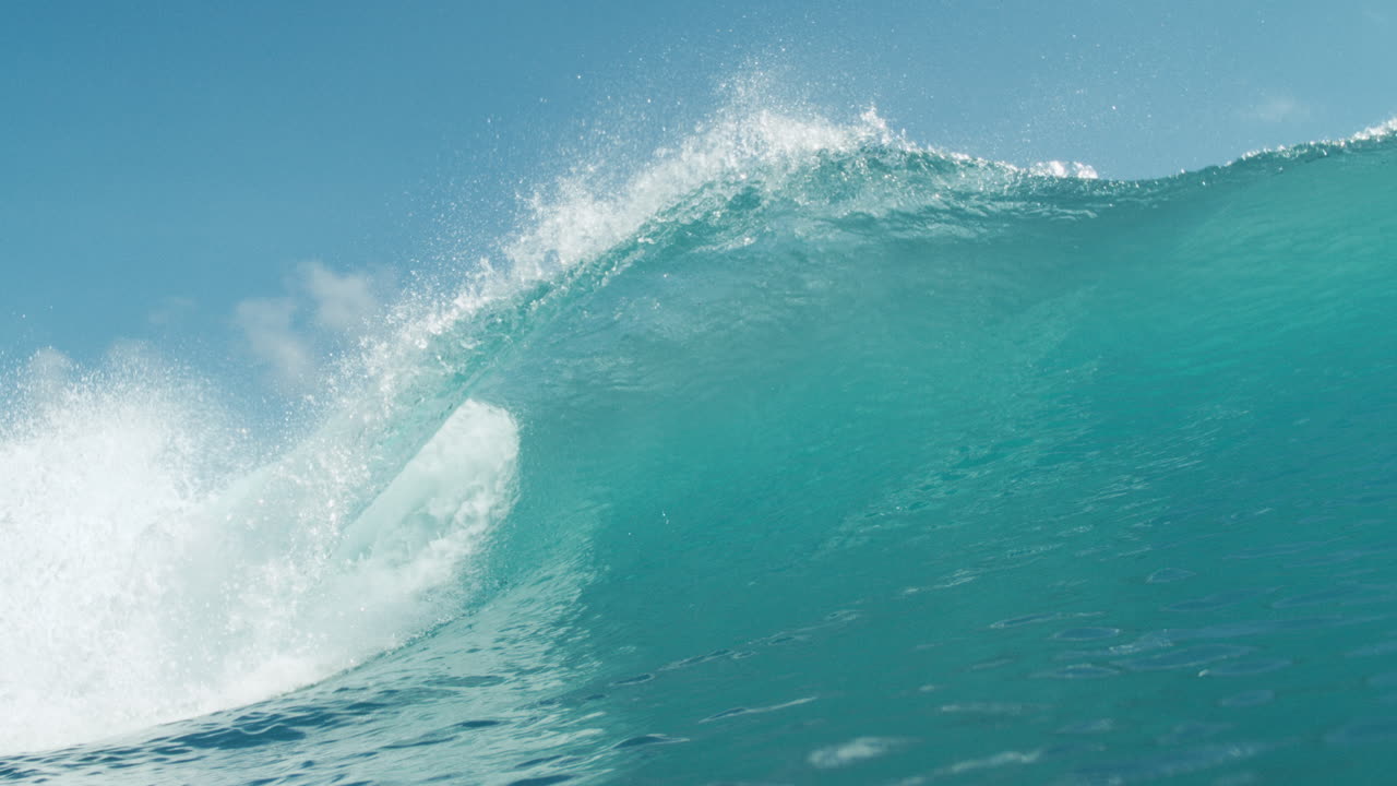 Curling ocean wave crashes in stunning slow motion with sunlit sky above
