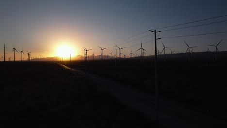 aerial view of sunset above wind turbines aray and cars moving on road, silhouettes and sun as backlight, cinematic drone shot