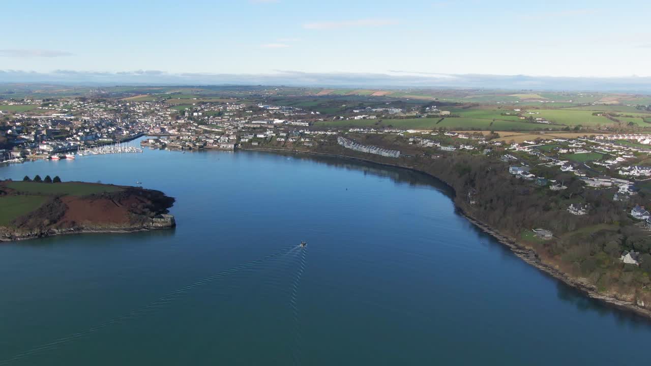 Aerial flight towards Kinsale harbour over calm waters with single boat on approach in center