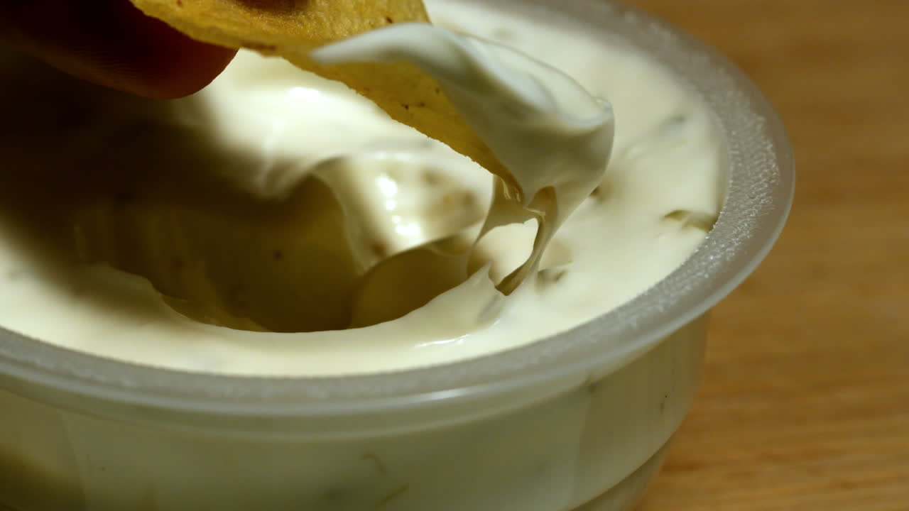 Mano che intinge una patatina in una salsa cremosa