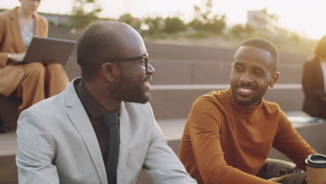 two cheerful african american businessmen talking over coffee in park