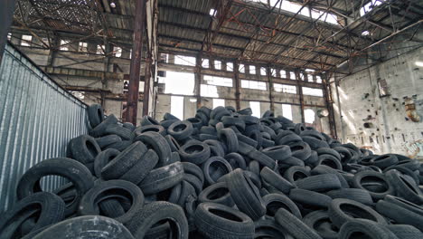 big pile of automobile tires on the broken-down plant with holes in the wall and roof. many black rubber tyres on the ground inside the old huge empty building. motion camera bottom up.