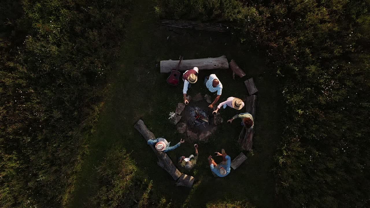 성숙 한 친구 들 이 야외 캠핑장 에서 불 을 둘러싸고 앉아 토스트 를 만드는 드론  ⁇