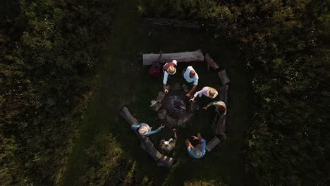 drone shot of mature friends making toast as they sit around fire at outdoor campsite