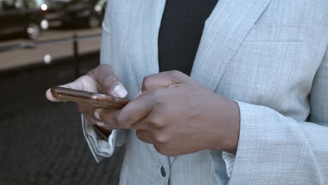 primer plano de una empresaria afroamericana irreconocible parada afuera y escribiendo un mensaje de texto en el teléfono celular