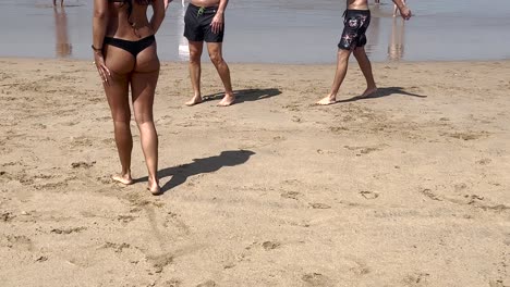 fit-woman-in-black-bikini-talking-with-hear-friends-by-the-beach-with-yellow-sand-in-slow-motion