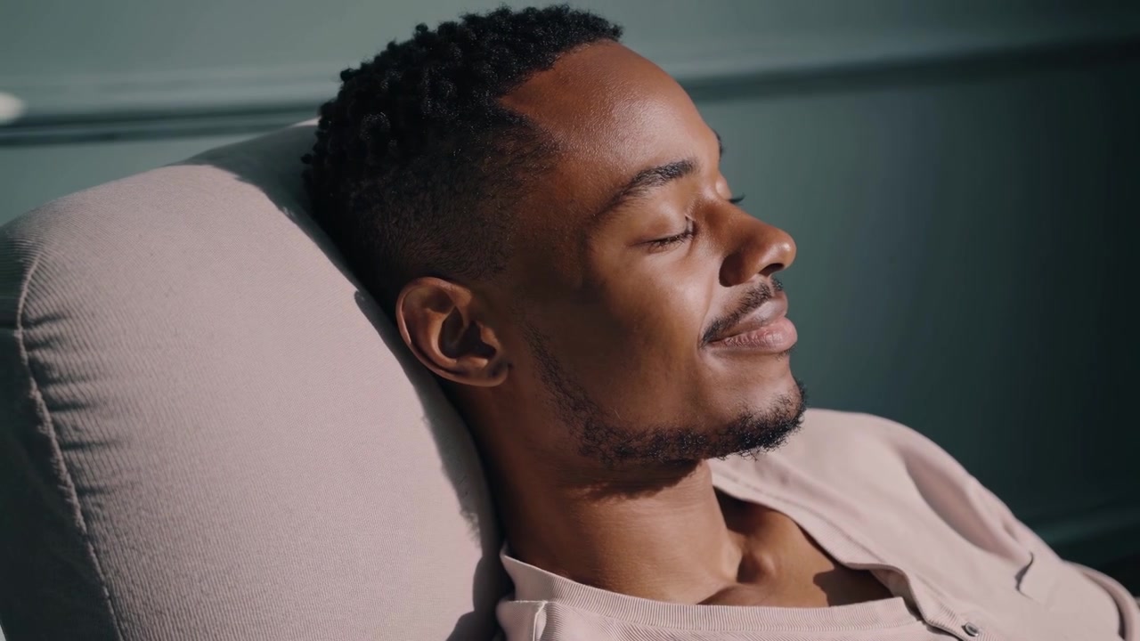 Ung afroamerikansk mann som slapper av i et solfylt rom med planter