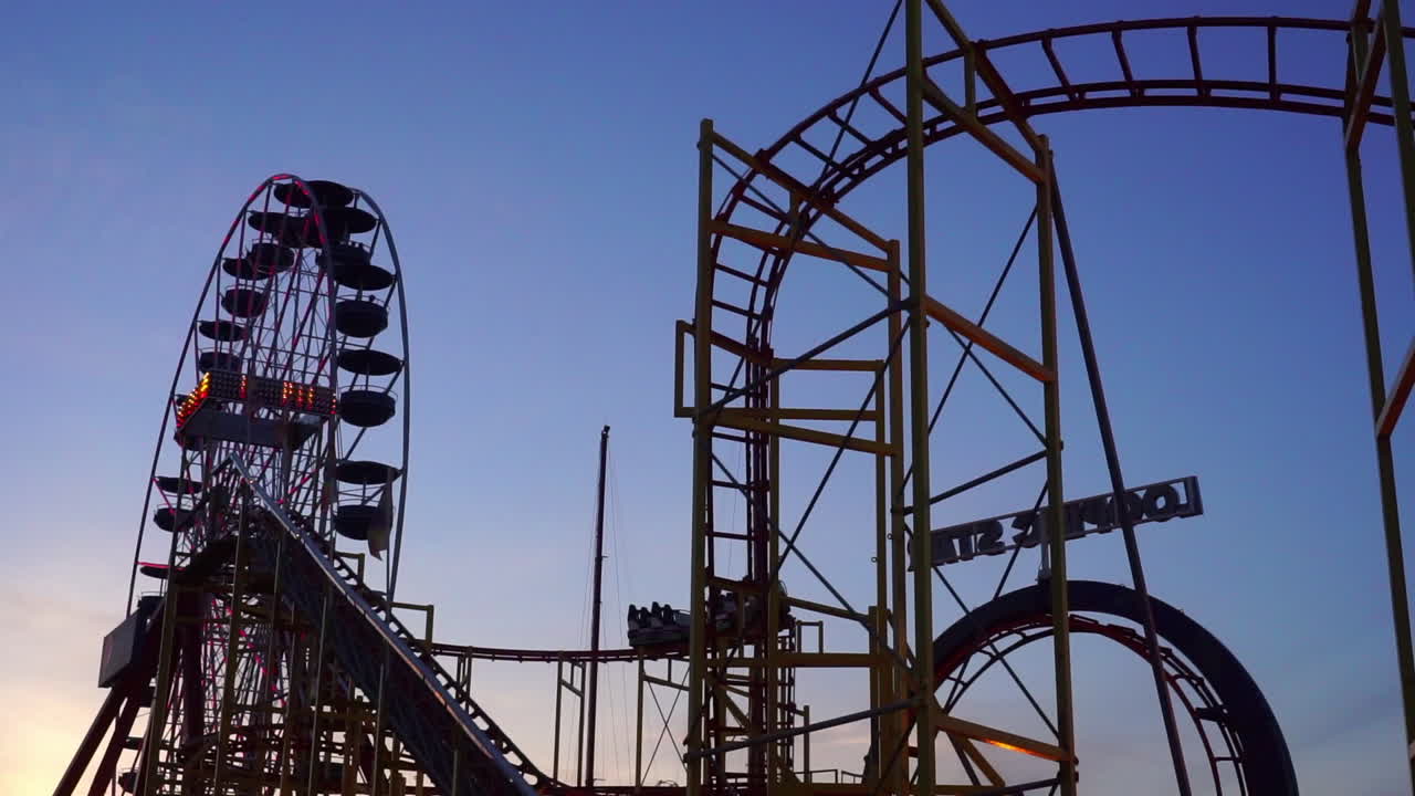 Uma roda-gigante, um brinquedo de bungee jump e uma montanha-russa com looping em um parque de diversões ao anoitecer