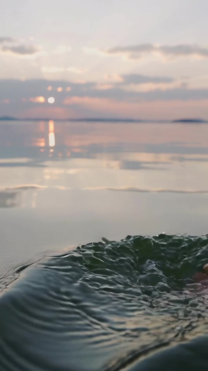 Verticale video: Blootvoets en onderbeen van een persoon dat in het meer zakt bij zonsondergang, rimpelingen creërend.